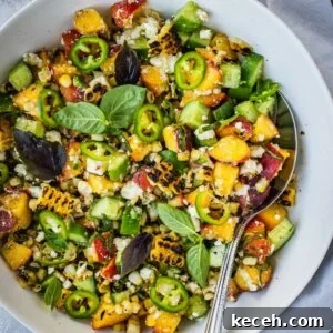 Grilled corn and peach summer salad with chopped cucumber and crumbled feta in a bowl garnished with jalapeno pepper rings and basil leaves.
