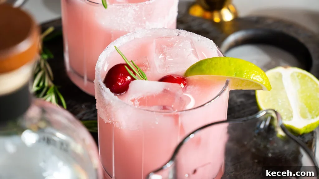 Cranberry Coconut Lime Christmas Margarita Recipe 2 A Christmas margarita recipe in a glass, with a lime wedge, cherries and ice.