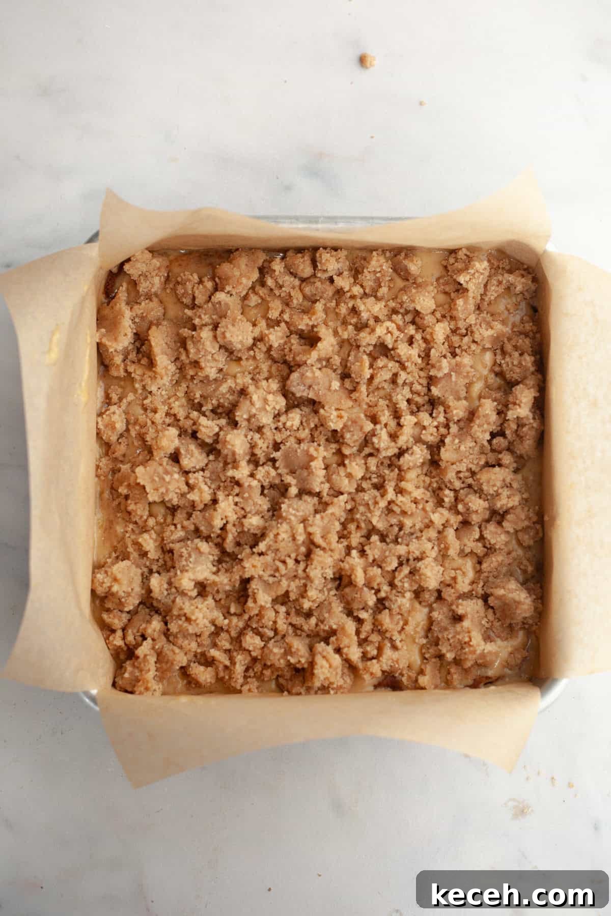 Moist Banana Coffee Cake with Sour Cream Glaze 9 A square baking pan lined with parchment paper and filled with cake batter, topped with streusel.