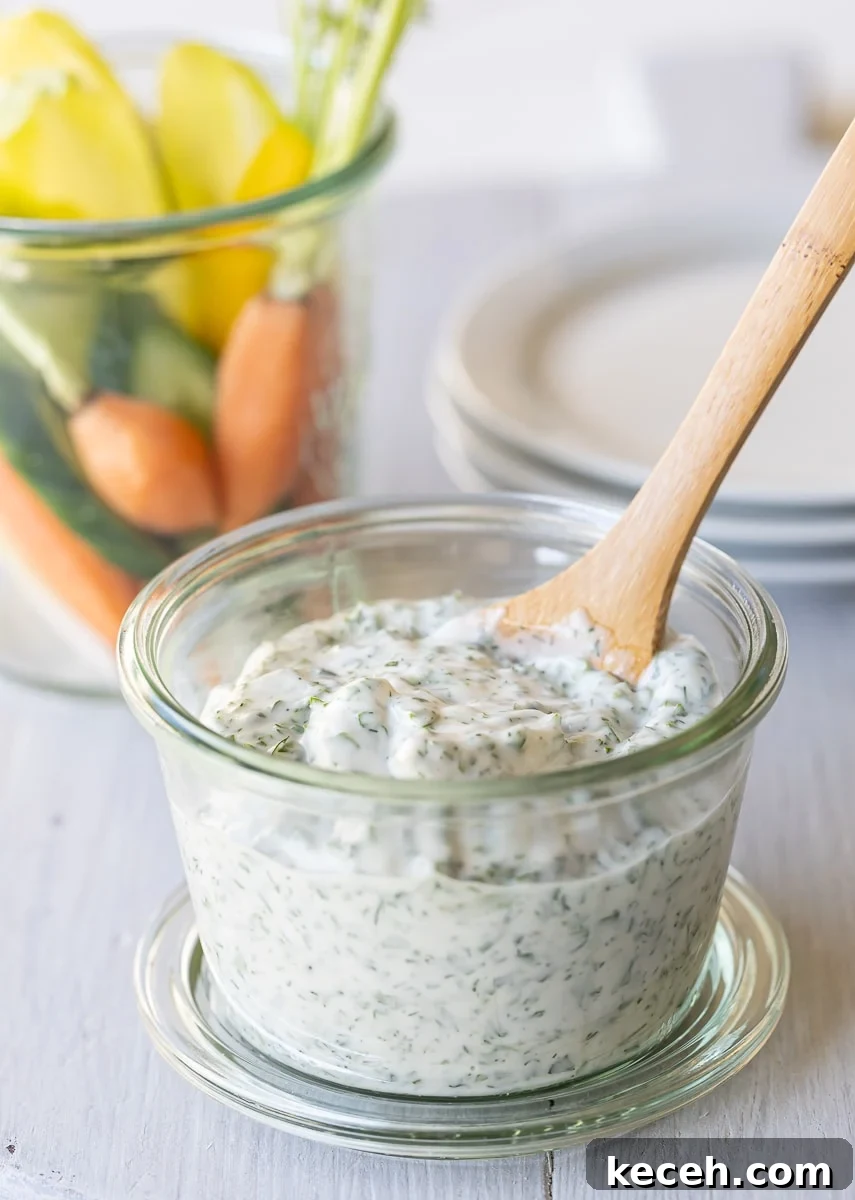 Creamy Green Goddess Dressing & Herb Dip Recipe 2 A jar of Green Goddess dip with a wooden spoon, small plates, and raw veggies.