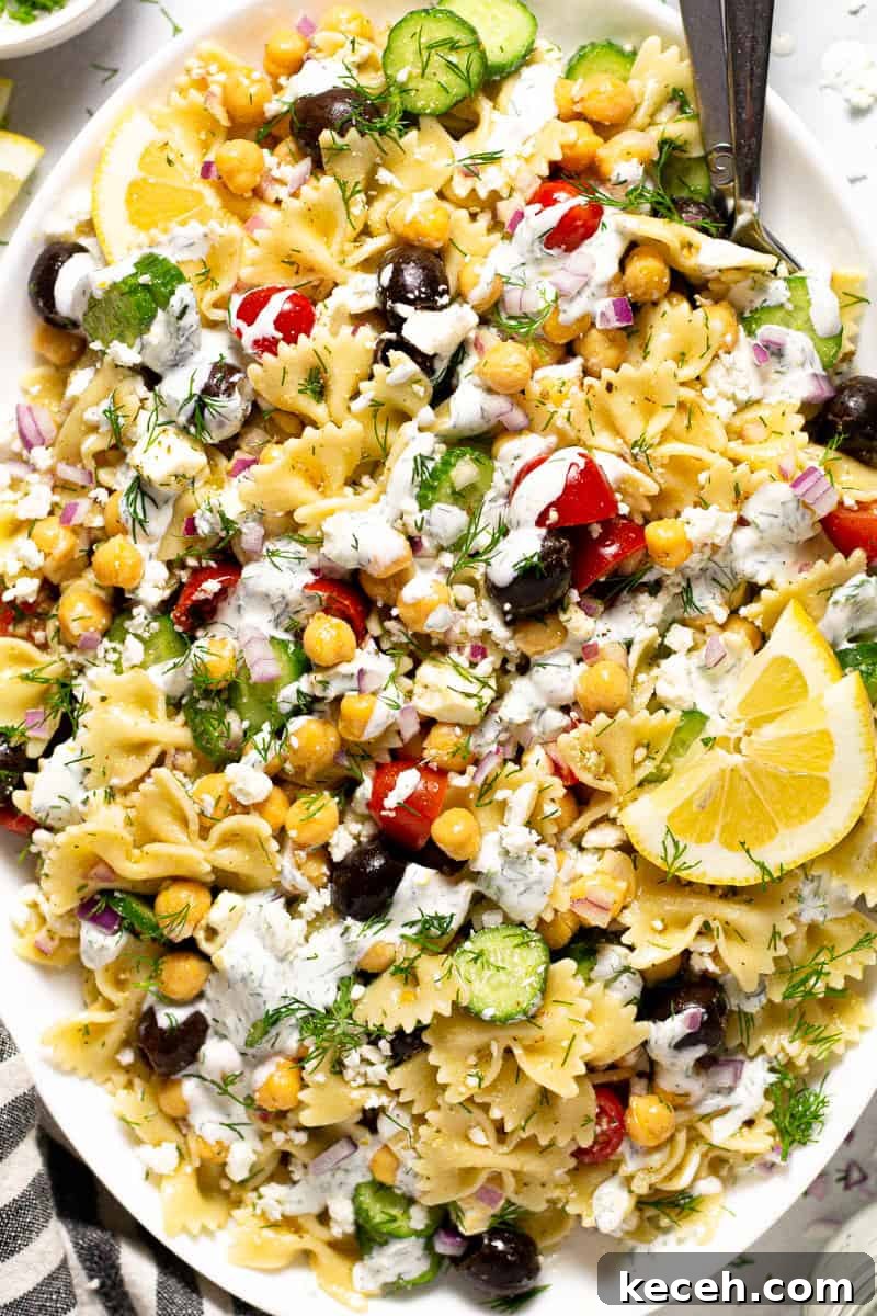 Overhead shot of a large white platter of chickpea pasta salad drizzled with yogurt sauce
