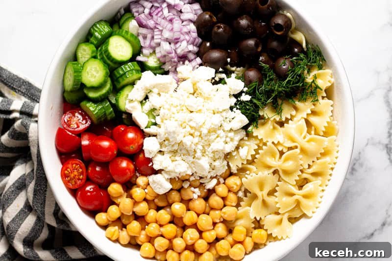 Overhead shot of a large white bowl filled with ingredients to make chickpea pasta salad
