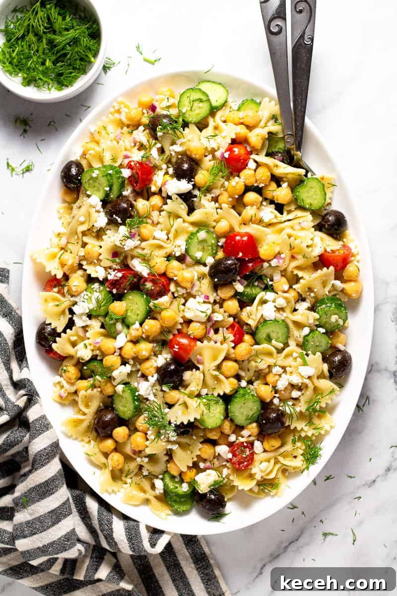 Overhead shot of a large white platter of chickpea pasta salad garnished with fresh dill 