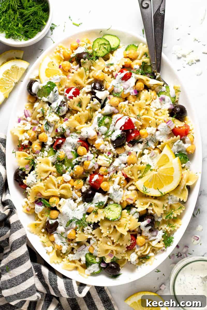 Overhead shot of a large white platter of chickpea pasta salad drizzled with yogurt sauce