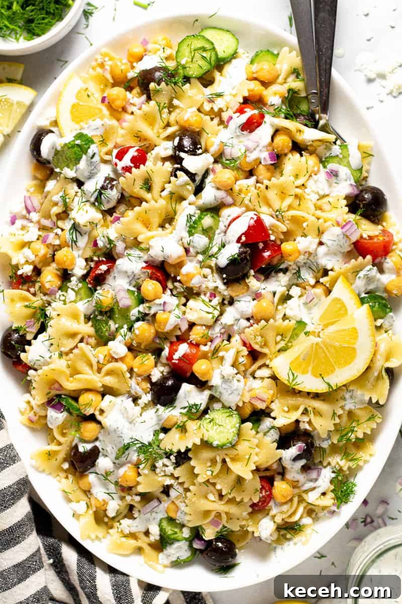 Overhead shot of a large white platter of Greek pasta salad drizzled with yogurt sauce