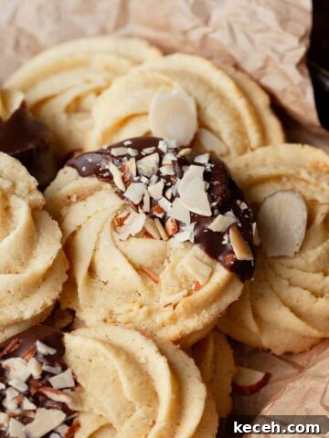 gluten free butter cookies dipped in dark chocolate and garnished with some chopped up almonds on brown parchment paper