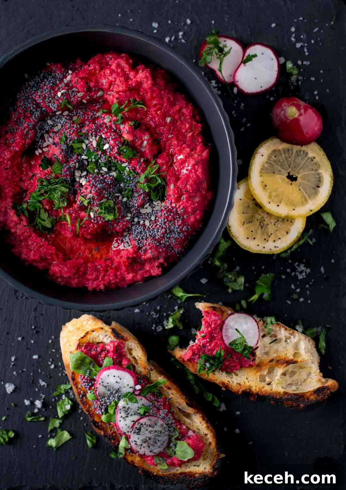 Creamy Beetroot Hummus Recipe — Vibrant and Simple Dip 2 Beetroot hummus in a black bowl with toasted bread and lemon slices on the side.