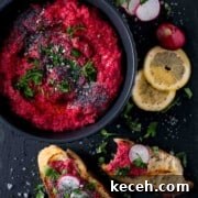 Creamy Beetroot Hummus Recipe — Vibrant and Simple Dip 8 Beetroot hummus in a black bowl with toasted bread and lemon slices on the side.