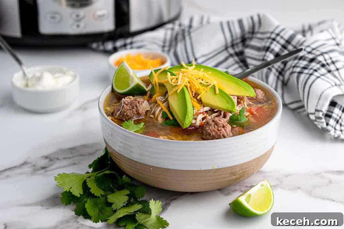 13 Delicious Low-Carb Mexican Recipes Worth Trying 13 A bowl of Mexican taco soup topped with avocado slices, shredded cheese, and cilantro sits on a marble counter near a lime wedge, cilantro leaves, sour cream, and a slow cooker.