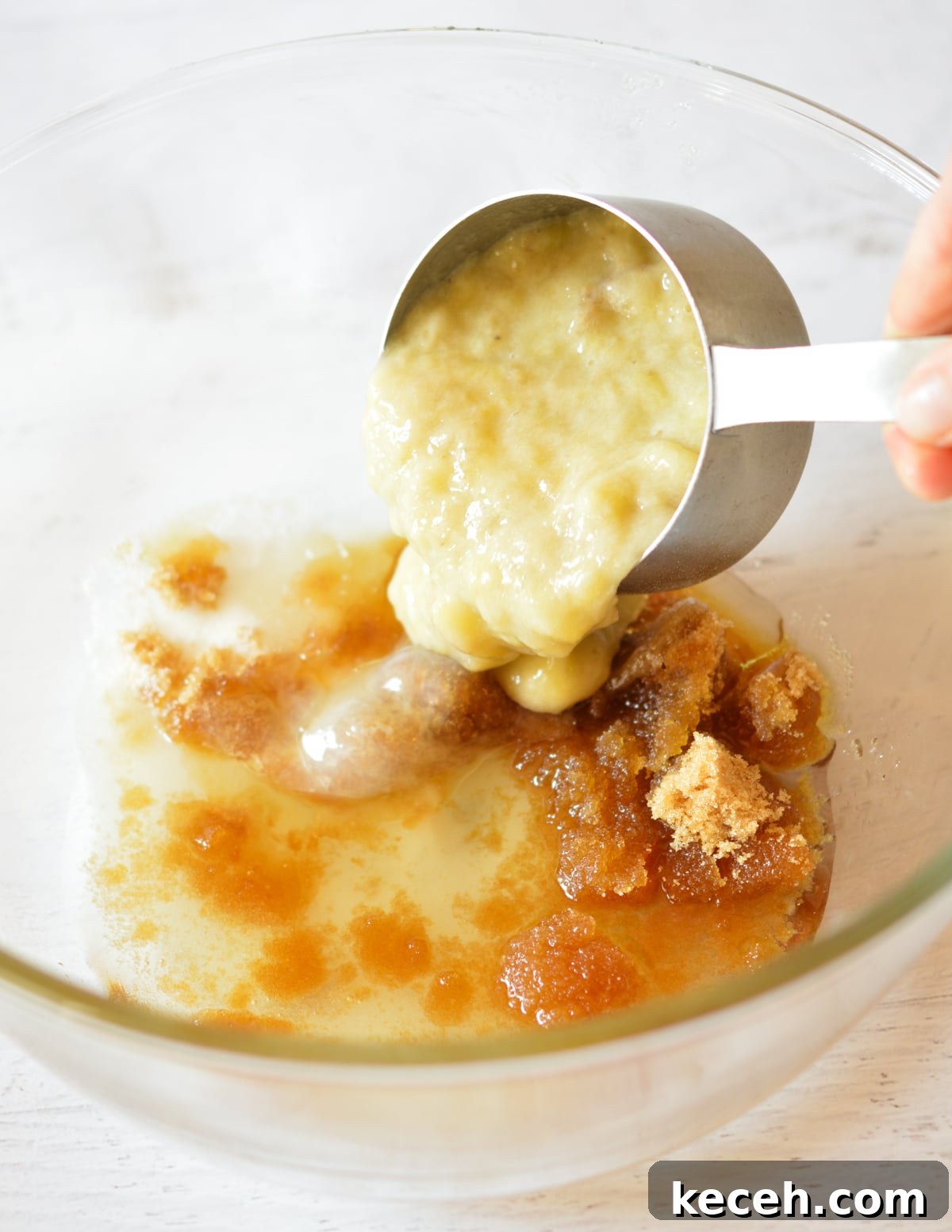 Moist Banana Bread Made with Frozen Bananas 7 pouring mashed banana into a bowl of sugar and brown sugar.