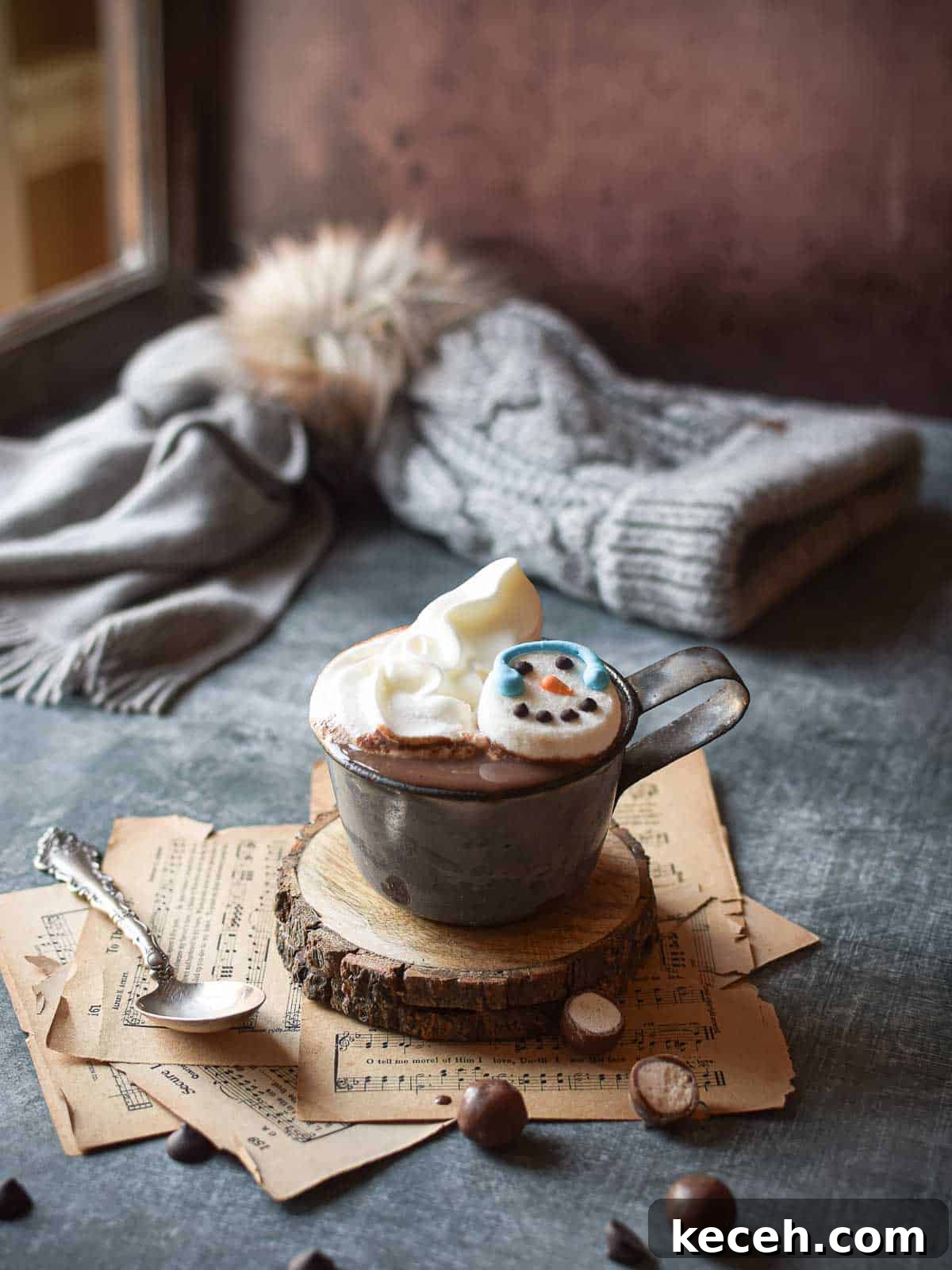 Hot chocolate scene by a window with a hat and scarf in the background and scattered malted milk balls.