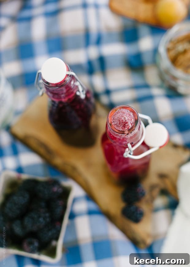 Blackberry Shrub Syrup in glass bottles surrounded by blackberries.