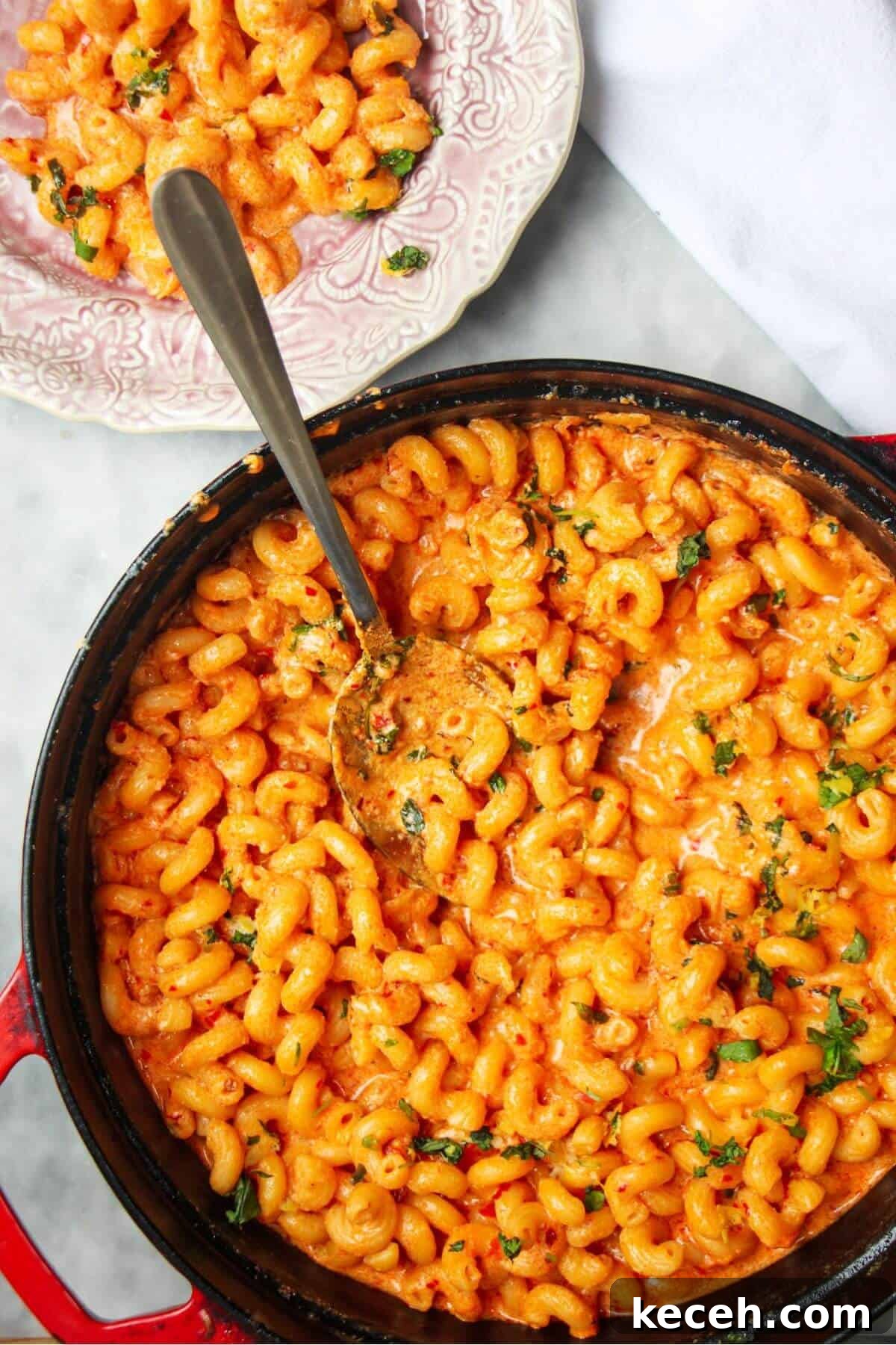 Creamy Spicy One-Pot Mac and Cheese Recipe 2 Spicy mac and cheese in a large black skillet with a silver spoon inside and pink plate next to it.