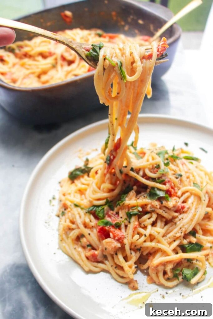 Creamy Spicy One-Pot Mac and Cheese Recipe 11 A fork pulling up baked burrata and tomato pasta with dish of pasta in the background.
