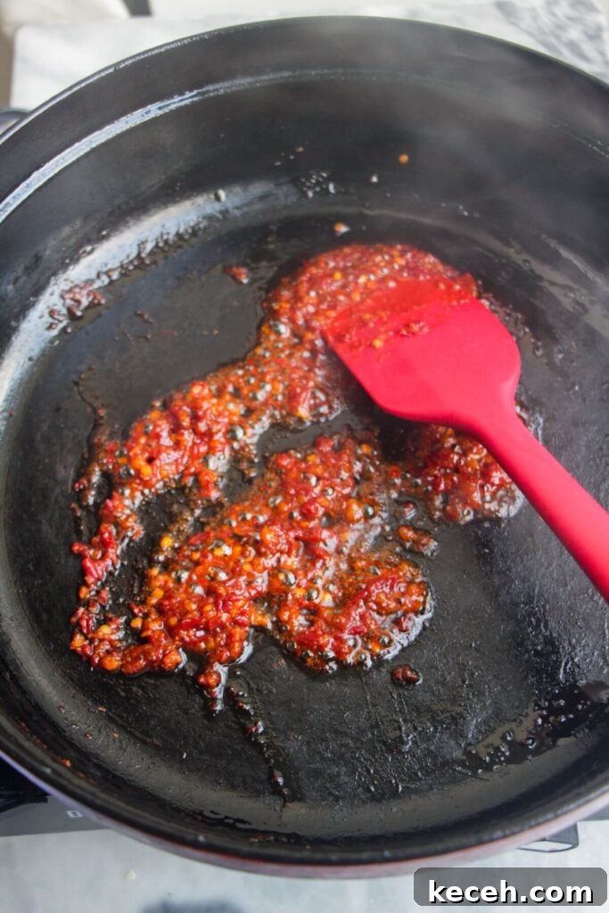 Creamy Spicy One-Pot Mac and Cheese Recipe 5 Red spatula stirring 'nduja paste in a large black skillet.