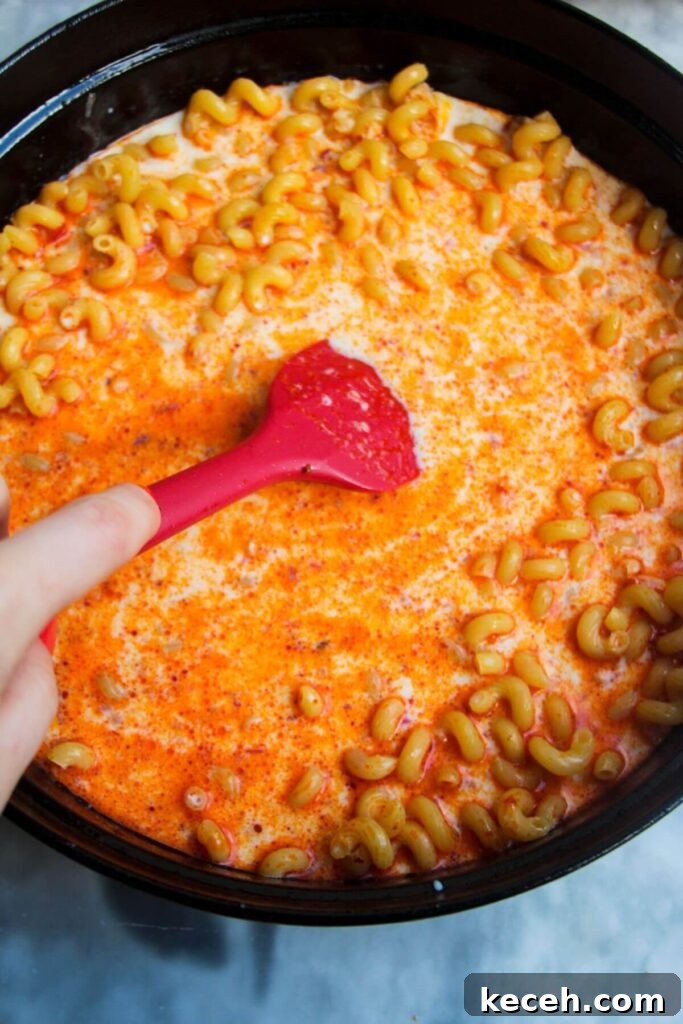 Creamy Spicy One-Pot Mac and Cheese Recipe 7 Red spatula stirring mac and cheese in a large black skillet.