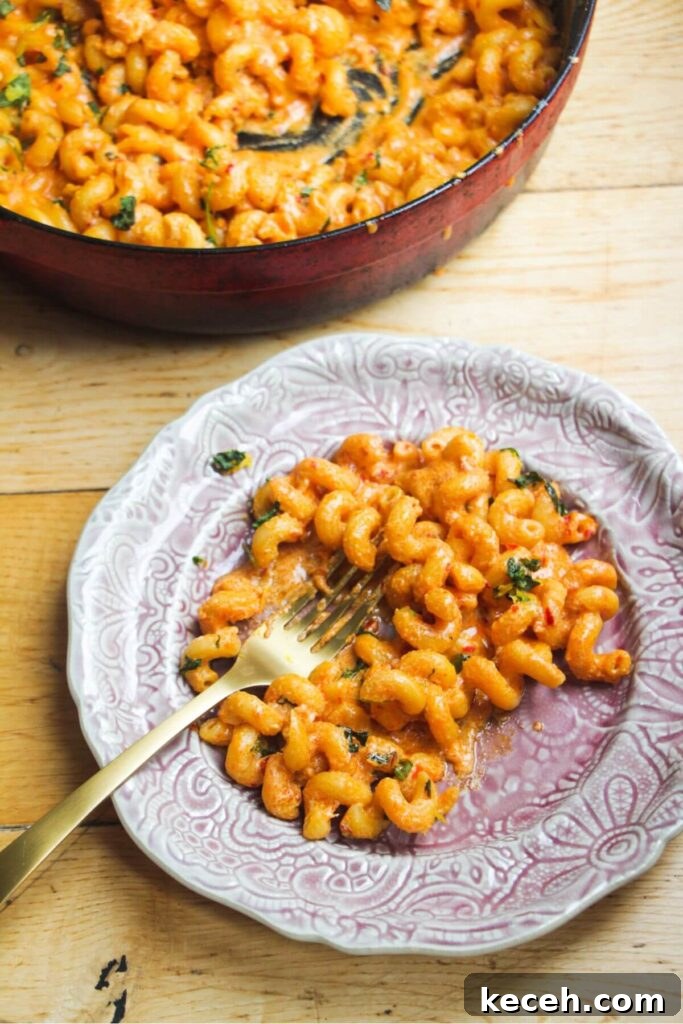 Creamy Spicy One-Pot Mac and Cheese Recipe 10 Spicy mac and cheese on a small pink plate with a skillet with more mac and cheese in the background.