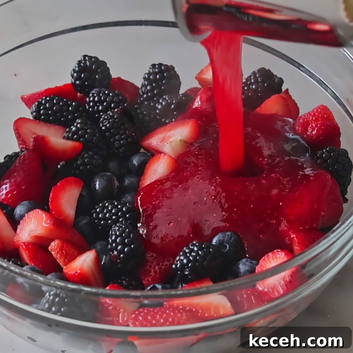 Gluten-Free Mixed Berry Pie Recipe — Fresh Summer Dessert 8 pouring jello mixture over fresh berries in large glass bowl.