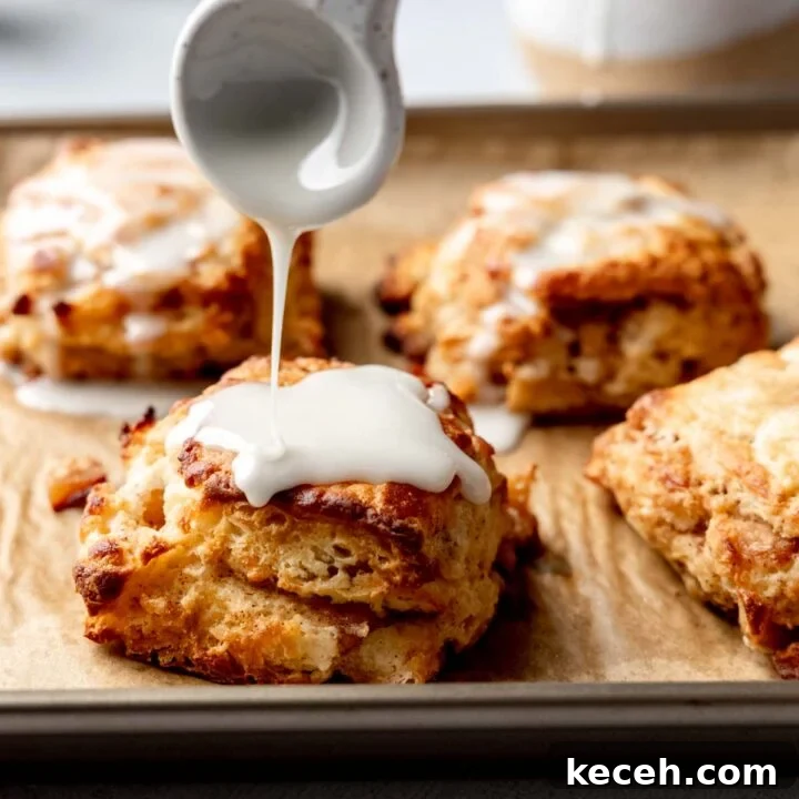 Spoon drizzling glaze over a warm gluten-free apple biscuit on a baking sheet with more biscuits in the background.