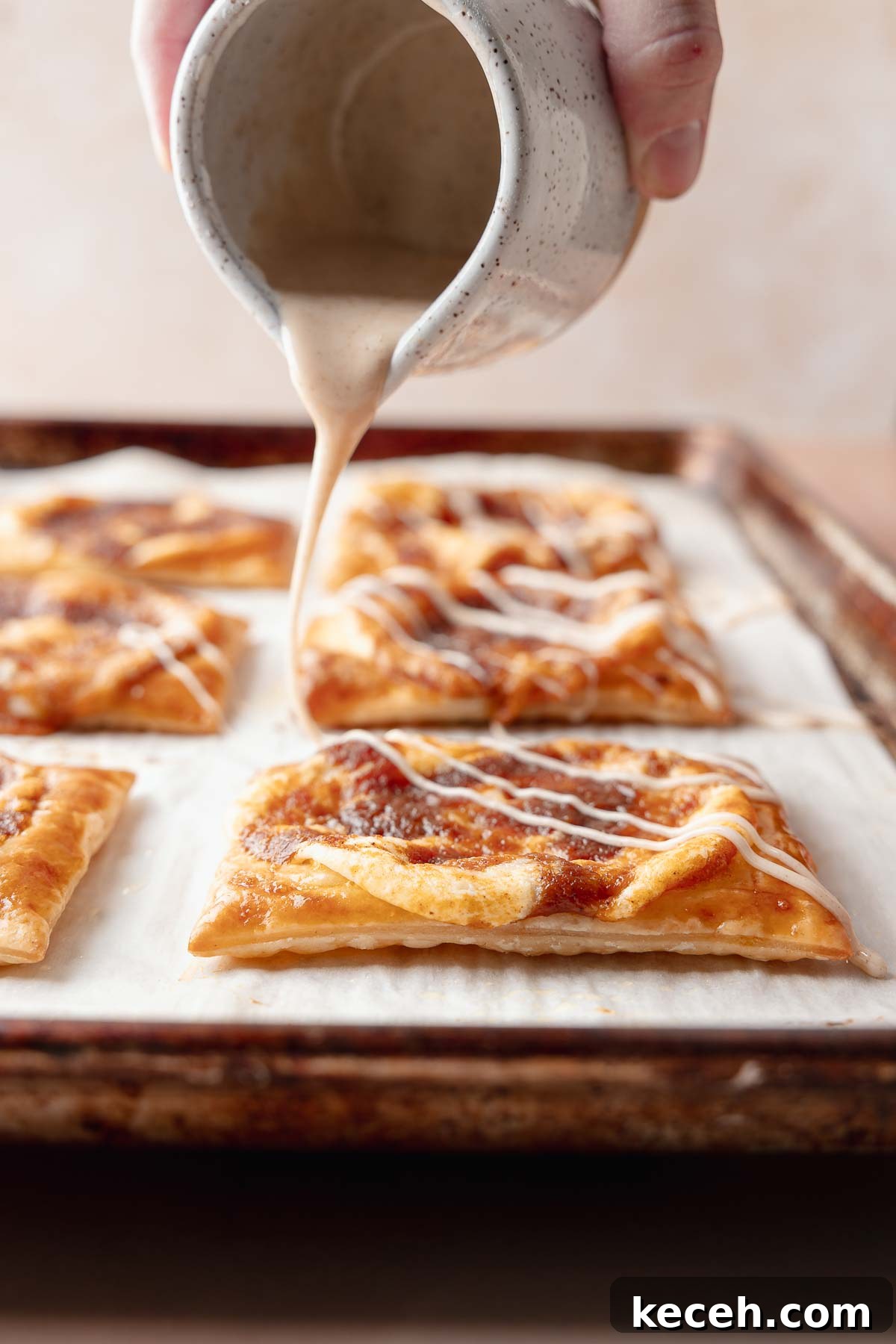 Gluten-Free Pumpkin Cream Cheese Danish Recipe — Starbucks Copycat 9 A hand drizzling glaze over freshly baked pumpkin danishes on the tray.