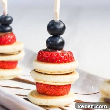 Small skewers holding bite-sized pancakes, strawberries, and blueberries arranged vertically on a white plate.