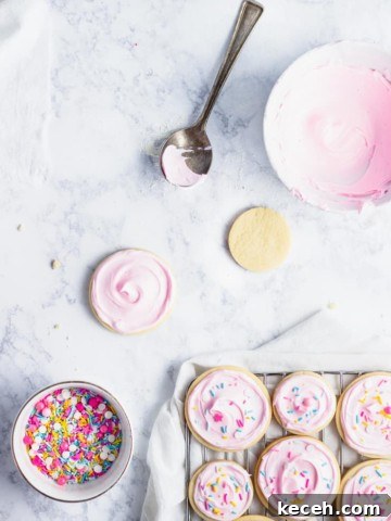 frosted cut out sugar cookies on a cooling rack with sprinkles and bowl of frosting in the background.