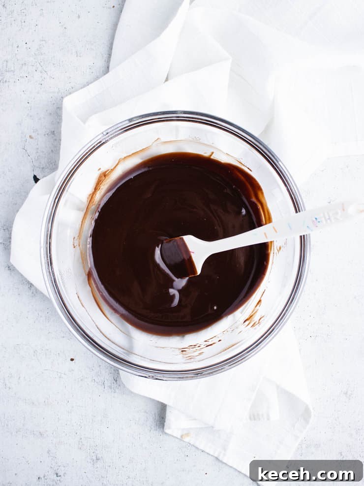 Chocolate Ganache Recipe: Smooth, Glossy Ganache in Minutes 7 Dark chocolate ganache in a clear bowl with a white spatula sticking out to the right.