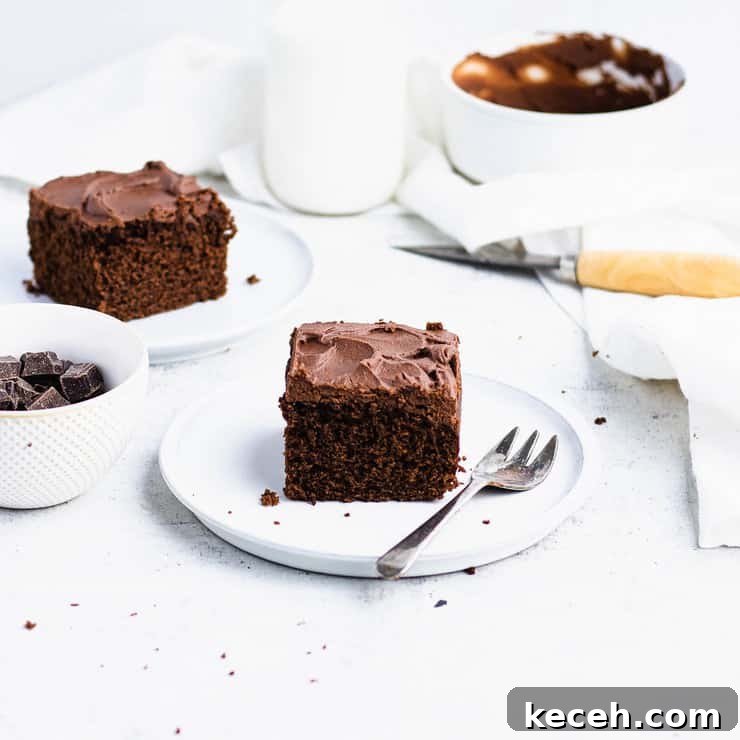 Chocolate Ganache Recipe: Smooth, Glossy Ganache in Minutes 10 Close up of a square slice of chocolate coffee cake with dark chocolate frosting on a white plate. A bowl of chocolate, a knife with a wooden handle, a bottle of milk and another plated slice are in the background.