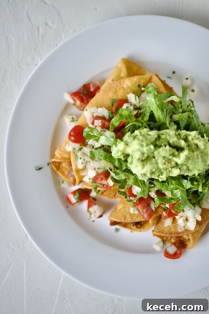 Flautas topped with pico de gallo, shredded lettuce, and avocado, ready to eat.