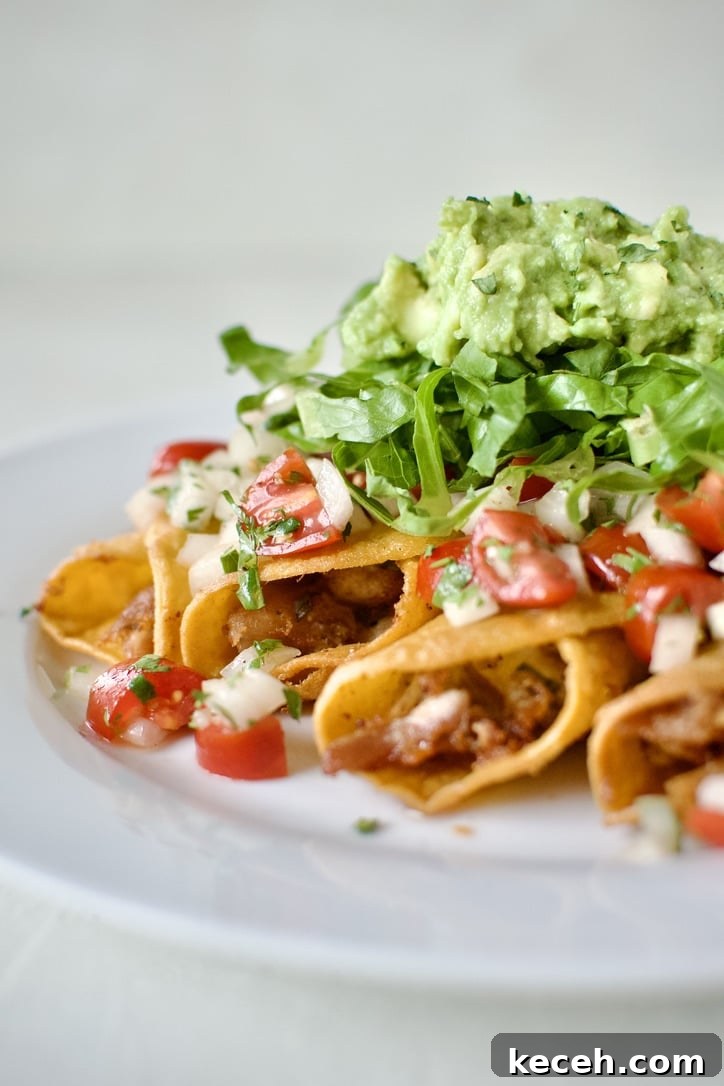 Flautas topped with pico de gallo, shredded lettuce, and avocado, ready to eat.