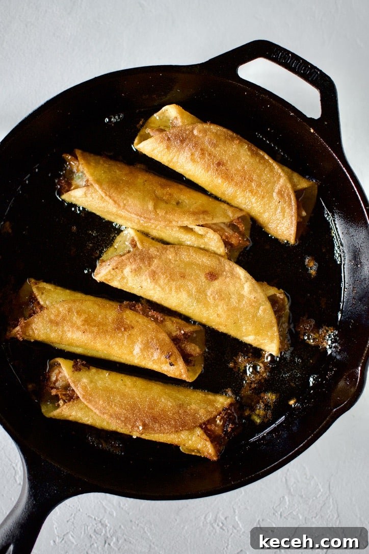 Flautas frying in a skillet in oil.