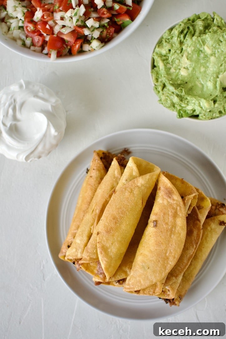 Cooked flautas stacked up on a plate cooling. Surrounded by optional toppings.