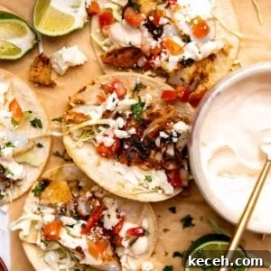 Fish tacos laying on parchment paper with lime wedges and a bowl of fish taco sauce.