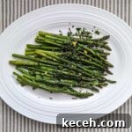Overhead shot of fresh, green roasted asparagus topped with mint gremolata on a white platter. The platter sits on a tray stripped tablecloth.
