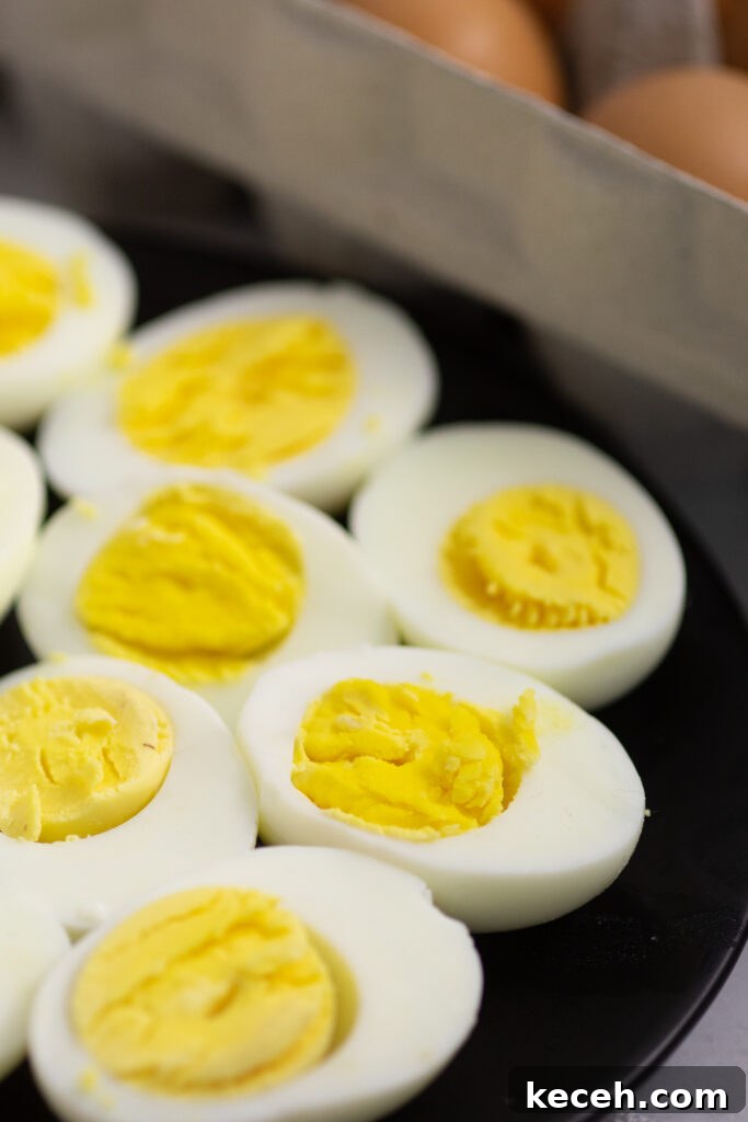 Hard boiled egg halves on a black plate with a carton of brown eggs behind.