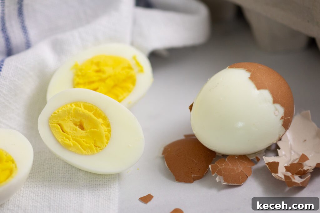 A hard boiled egg cut in half on the left and an egg half-peeled on the right with a linen napkin behind