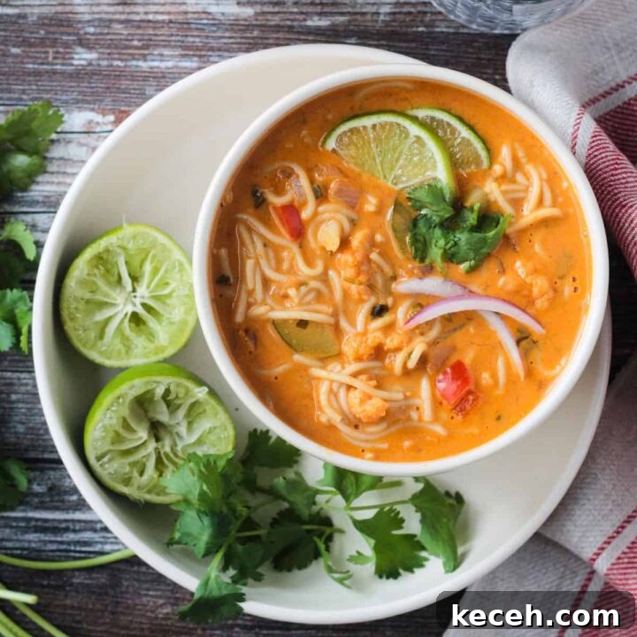 Red Curry Thai Noodle Soup in a white bowl next to two lime halves and cilantro leaves.