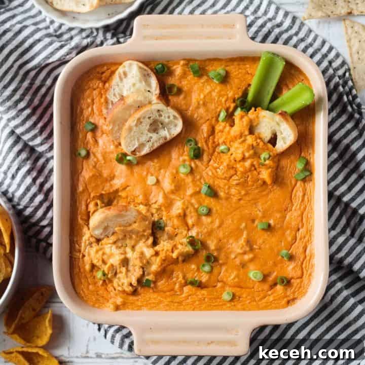 Baguette slices dipped in Vegan Buffalo Chicken Dip in a square baking dish topped with green onions.