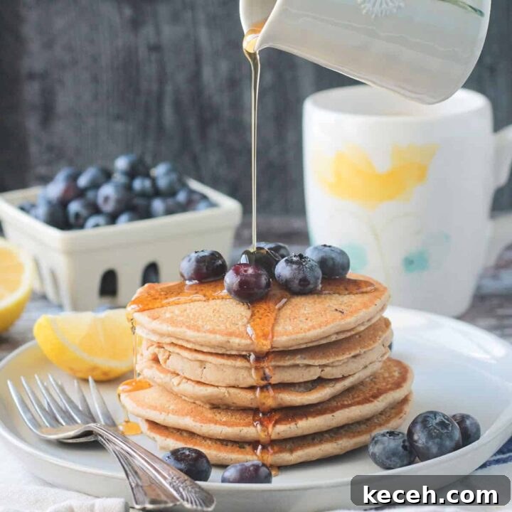 Syrup being poured onto a stack of 5 oat flour pancakes topped with blueberries.