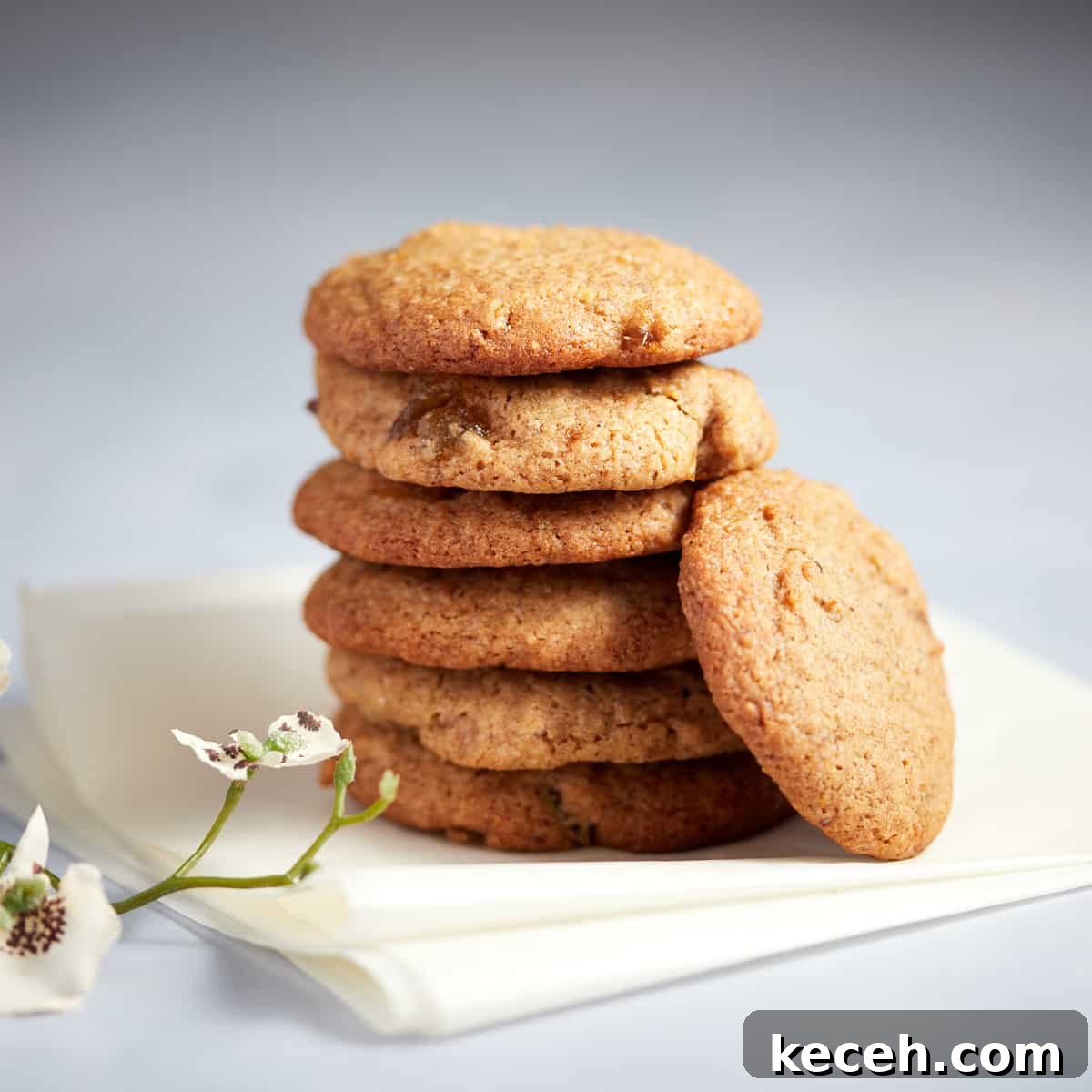 Photo of a stack of stem ginger cookies sitting on a white napkin with some flowers in front.
