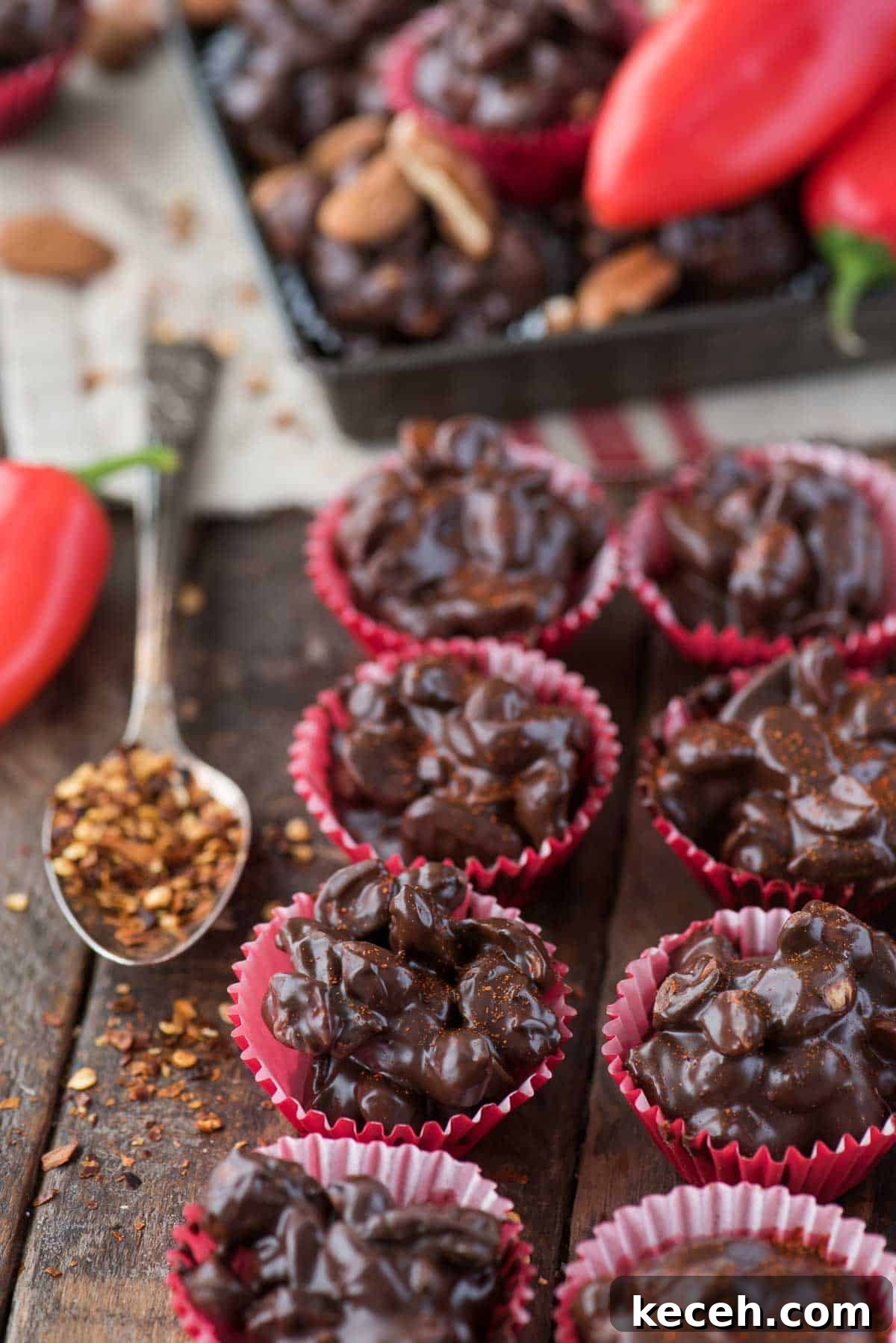 Crock pot or stove top spicy nut clusters! These dark chocolate cayenne nut clusters are popular during the holiday season. Plus there’s notes for making them less spicy or packed with heat! dark chocolate cayenne nut clusters in red mini muffin paper cups on wood background