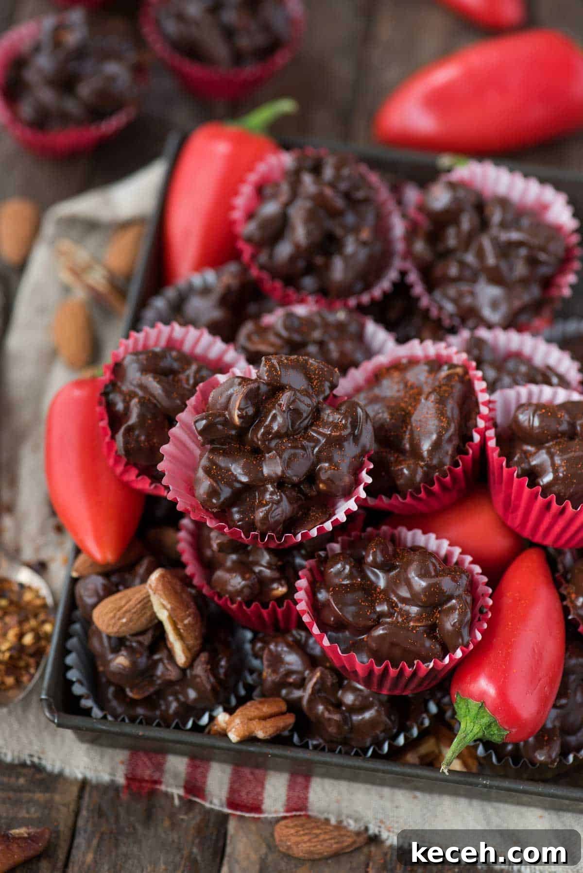 Crock pot or stove top spicy nut clusters! These dark chocolate cayenne nut clusters are popular during the holiday season. Plus there’s notes for making them less spicy or packed with heat! dark chocolate cayenne nut clusters in red mini muffin paper cups on wood background