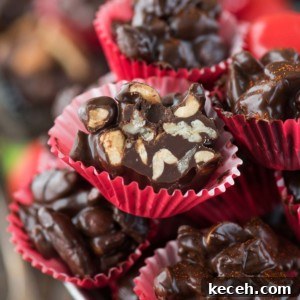 Dark Chocolate Cayenne Nut Clusters Recipe — Spicy Chocolate Bites 2 Close-up of glossy nut clusters of dark chocolate candy with nuts, placed in red and pink paper cups, stacked on a plate. Various nut pieces are visible inside the rich chocolate.