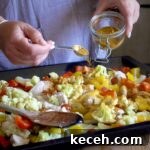 Curried Chicken Tray Bake Recipe from The Slimming Foodie 13 Woman in grey scattering a homemade spice blend over a baking tray of chopped veggies and chicken