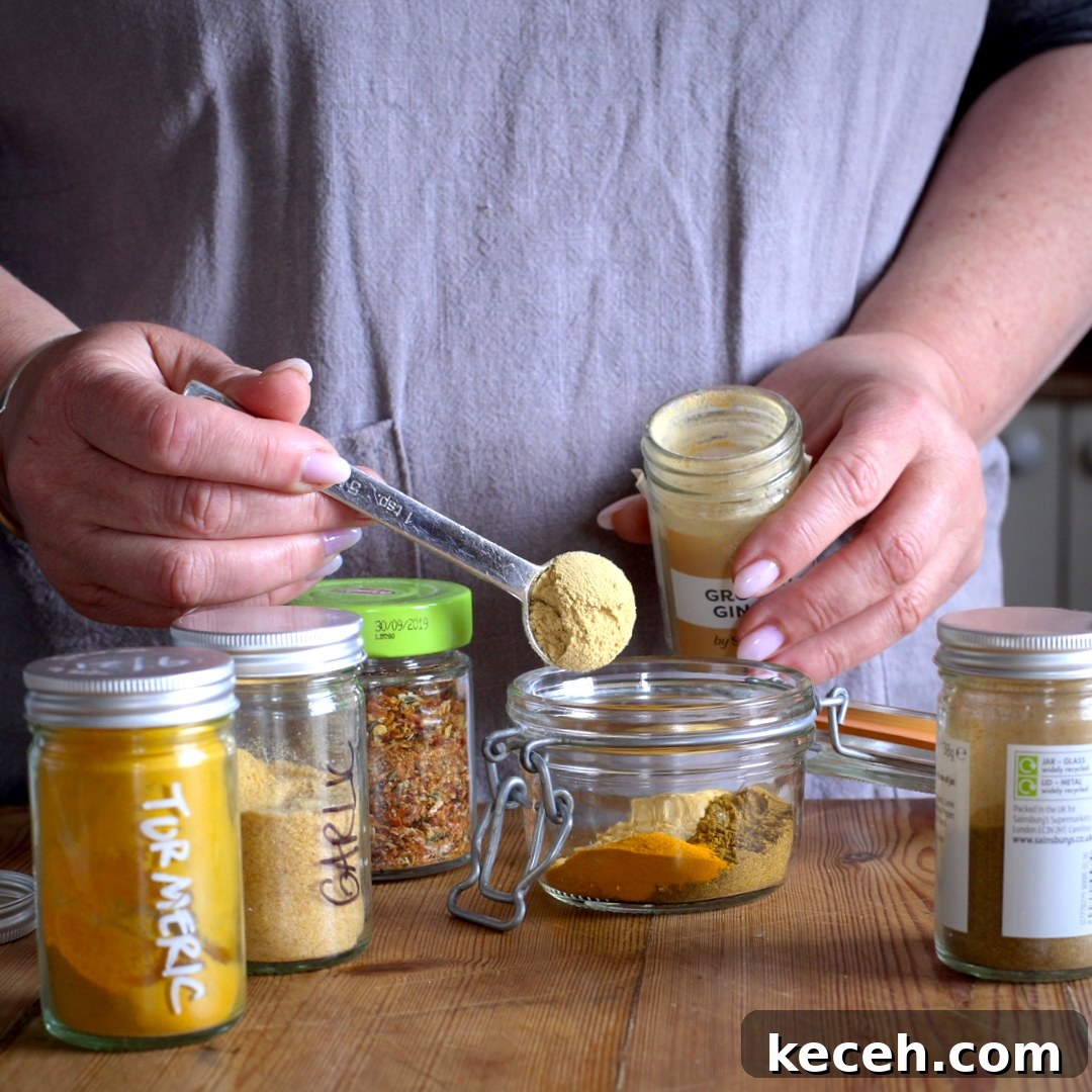 Curried Chicken Tray Bake Recipe from The Slimming Foodie 5 Woman in grey spooning various coloured spices from small glass pots into a glass jar