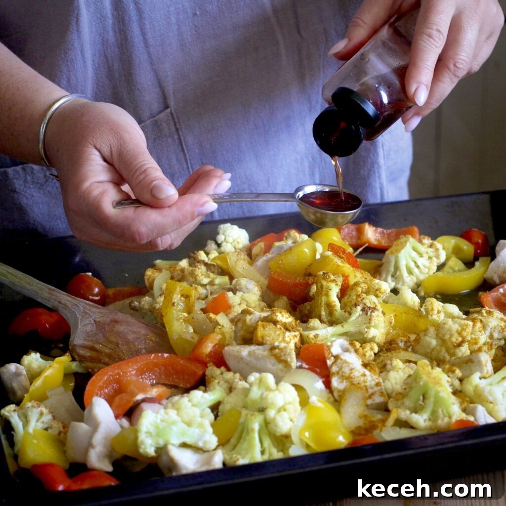 Curried Chicken Tray Bake Recipe from The Slimming Foodie 10 Woman measuring out red wine vinegar onto a sheet pan of chopped chicken and veggies
