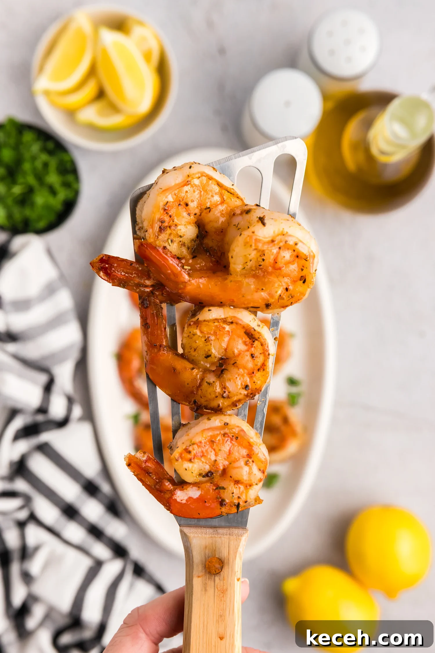 Crispy Blackstone Grilled Shrimp with Garlic Butter Sauce 11 Cooked shrimp resting on a metal spatula held above a serving plate with parsley garnish.