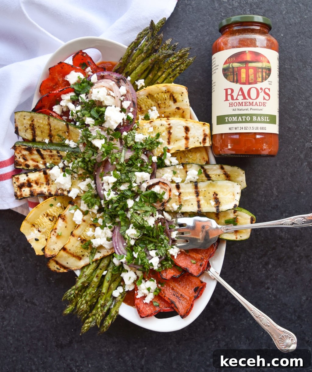 Platter of colorful grilled vegetables with serving utensils next to a full jar of Rao's Tomato Basil Sauce.