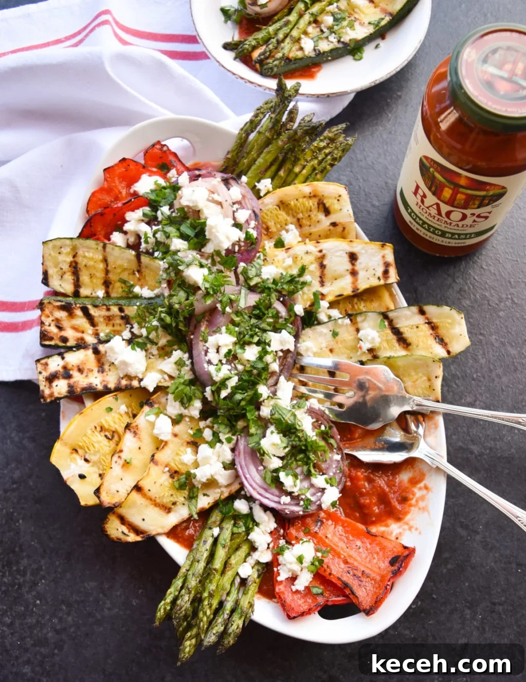 Platter of grilled vegetables with one portion removed and part of a plated serving in the top of the frame. 