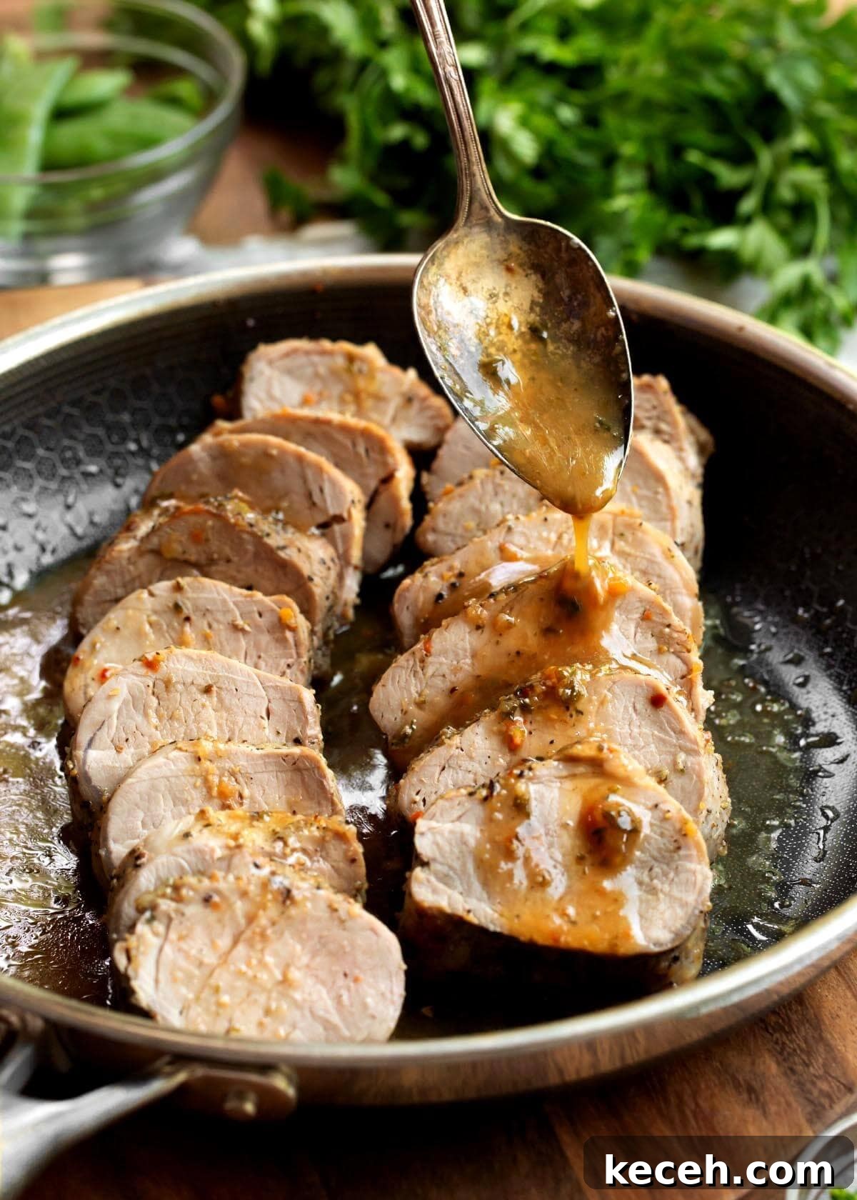 Oven-Roasted Pork Tenderloin Recipe 2 2 Pork Tenderloins sliced in a skillet with spoon drizzling sauce on them.